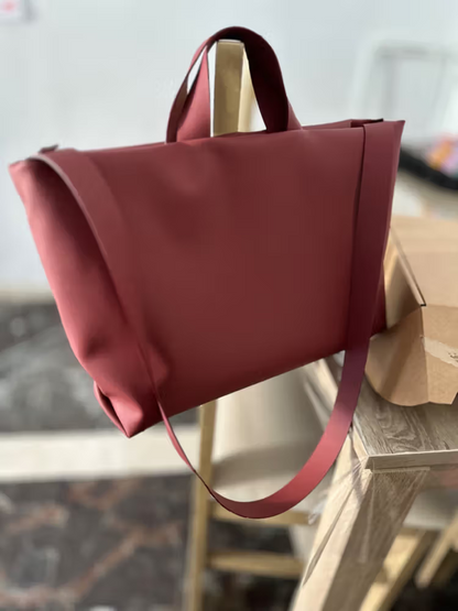 Sac Juanita en cuir bordeaux, suspendu par ses poignées dans un atelier, avec sa bandoulière, Bmassy.