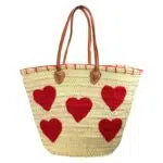 Panier en raphia beige naturel décoré de cœurs rouges, avec longues anses marron, sur fond blanc.