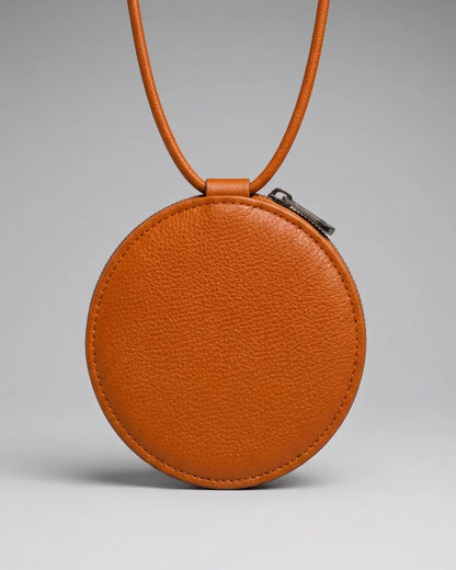 Mini sac rond en cuir orange Almita Mini porté avec sa bandoulière