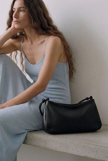 Sac MariLoli en cuir noir posé sur un banc à côté d’une femme assise