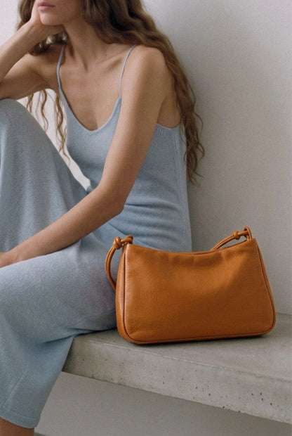 Sac MariLoli en cuir orange posé sur un banc à côté d’une femme assise