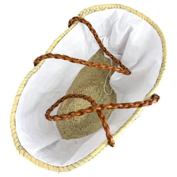 Panier en fibre naturelle beige vu de dessus, intérieur doublé de tissu blanc et poignées en cuir marron tressé.