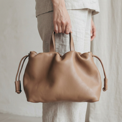 Petit sac à main Angelines en cuir beige sable tenu à la main par ses poignées, Bmassy.