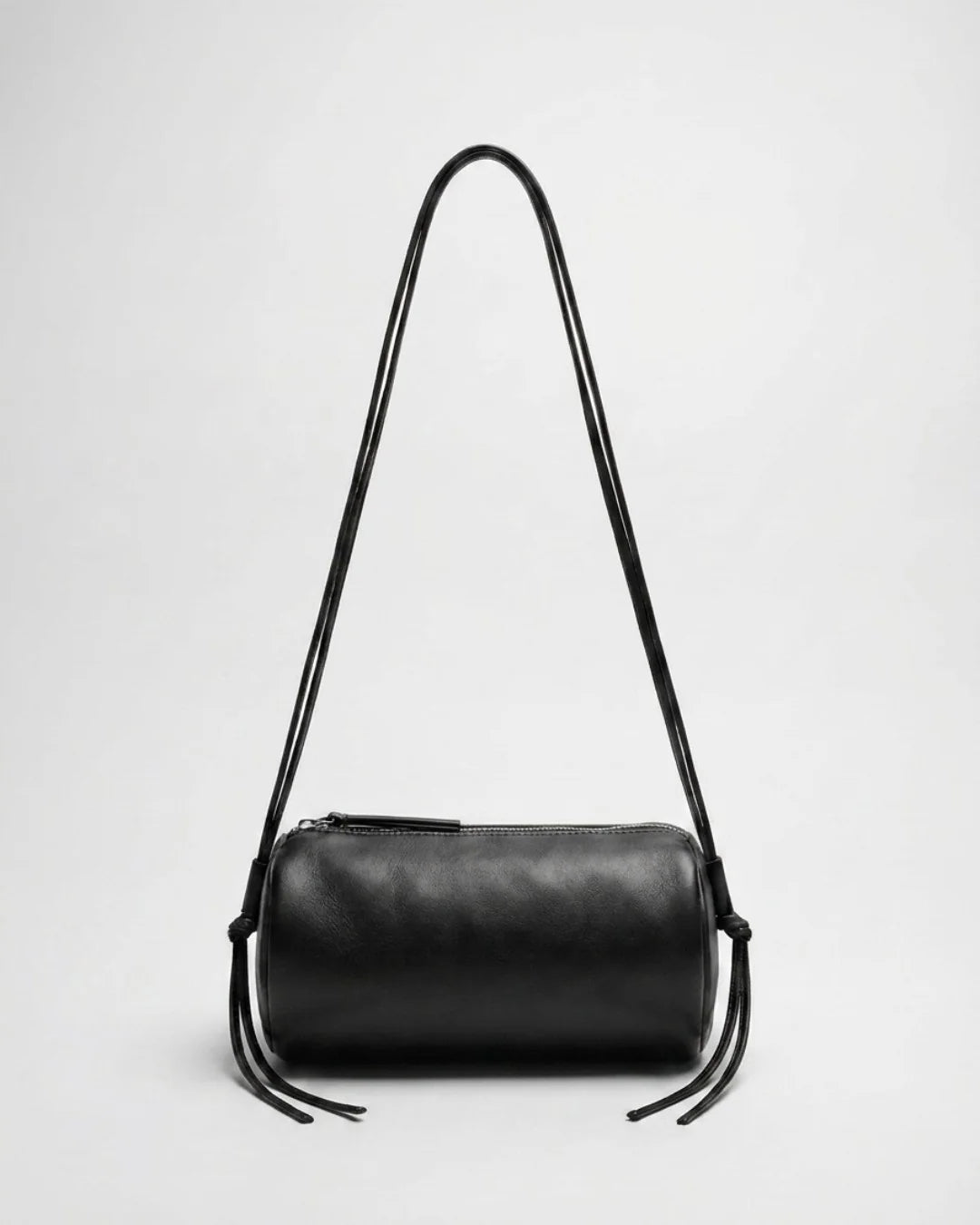 Sac Alma en cuir noir de forme cylindrique, présenté avec ses longs cordons relevés en bandoulière