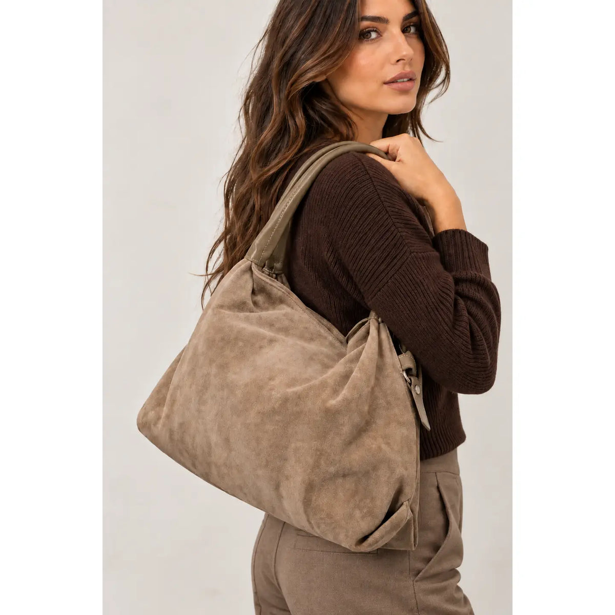 Sac Capucine en cuir velours taupe porté à l’épaule avec un pull brun et un pantalon