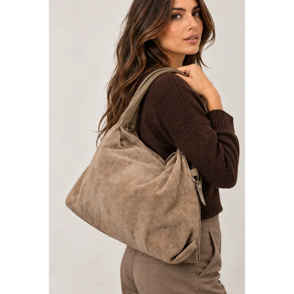 Sac Capucine en cuir velours taupe porté à l’épaule avec un pull brun et un pantalon