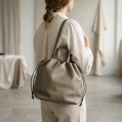 Sac à main Angela Medium en cuir gris taupe porté à l’épaule sur une femme vue de dos, Bmassy.