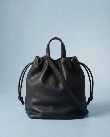 Sac à main Angela Medium en cuir noir vu de face avec sa bandoulière sur fond bleu clair, Bmassy.