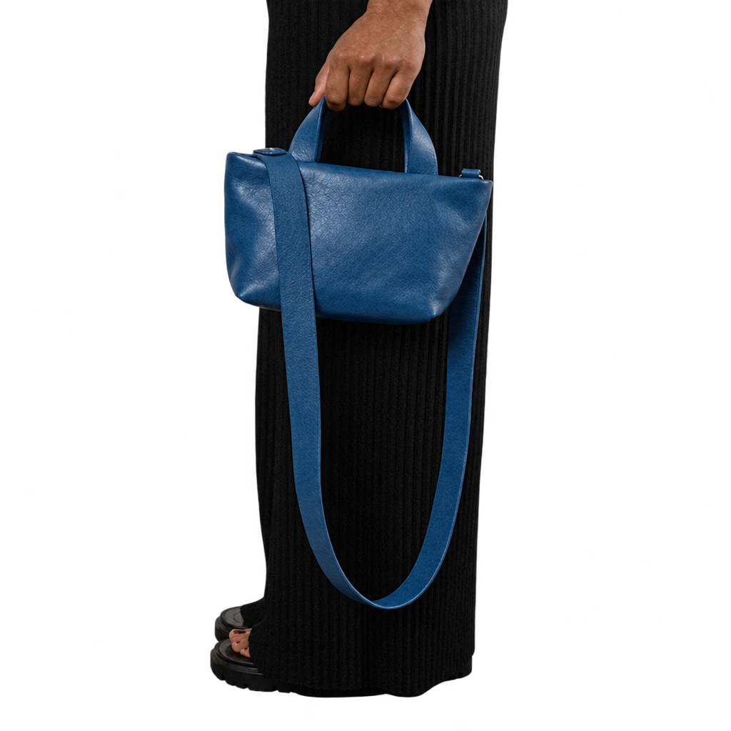 Sac Juanita en cuir bleu nuit, tenu à la main avec sa longue bandoulière visible, Bmassy.