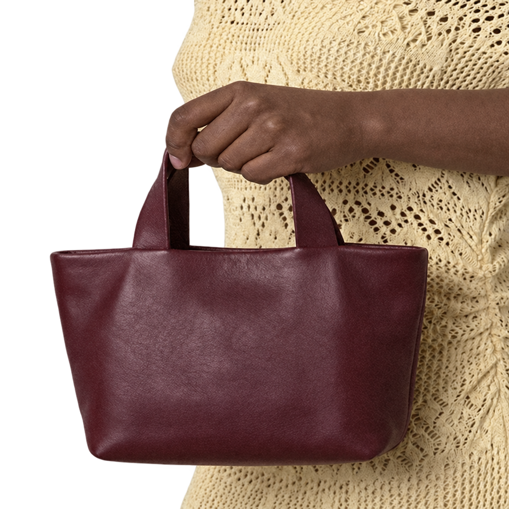 Sac Juanita en cuir bordeaux, tenu à la main par ses poignées devant une tenue écrue, Bmassy.