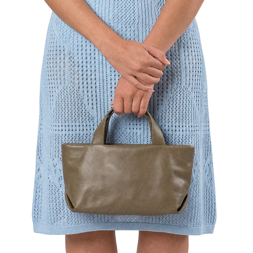 Sac Juanita en cuir gris, tenu à la main par ses poignées devant une robe bleu clair, Bmassy.