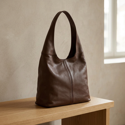 Sac à main marron à large anse et couture incurvée, posé sur un banc en bois clair