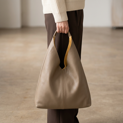 Sac shopper en cuir beige tenu à la main par son anse, avec intérieur ocre visible à l’ouverture