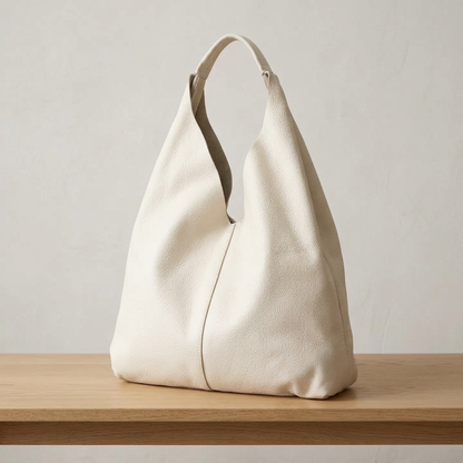 Sac shopper en cuir grainé blanc posé sur un banc en bois clair, vu de trois quarts