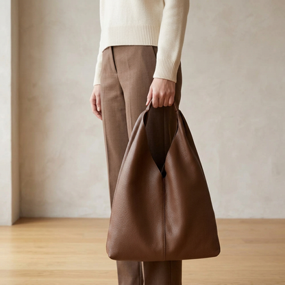Sac shopper en cuir grainé marron tenu à la main par son anse, le long de la jambe
