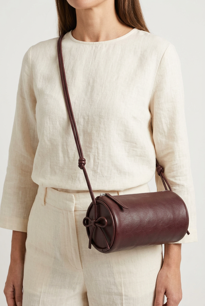 Sac Alma bordeaux de forme cylindrique, porté en bandoulière sur une tenue écrue