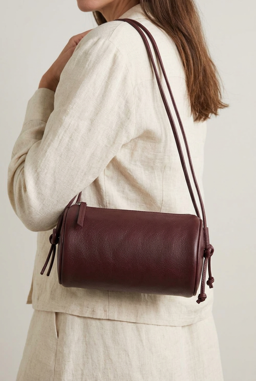 Sac Alma bordeaux de forme cylindrique, vu de trois quarts avec fermeture zippée et cordon noué sur le côté