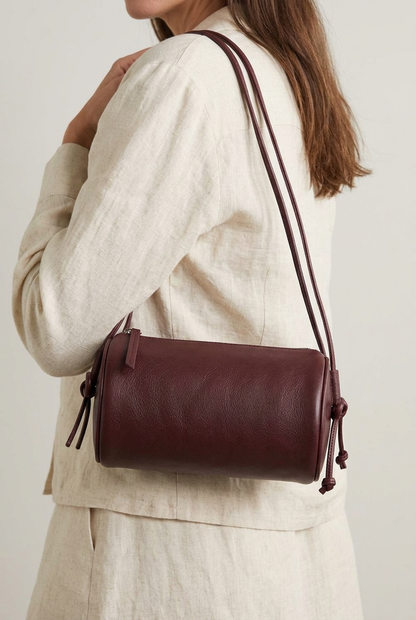 Sac Alma bordeaux de forme cylindrique, vu de trois quarts avec fermeture zippée et cordon noué sur le côté