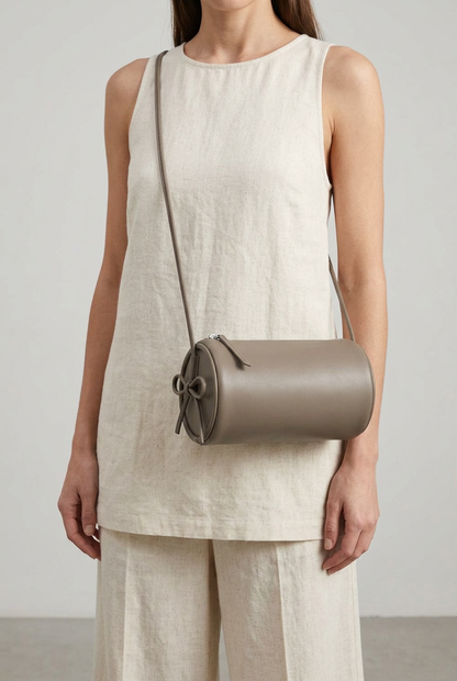 Sac Alma en cuir gris de forme cylindrique, porté en bandoulière devant par une femme en tenue écrue
