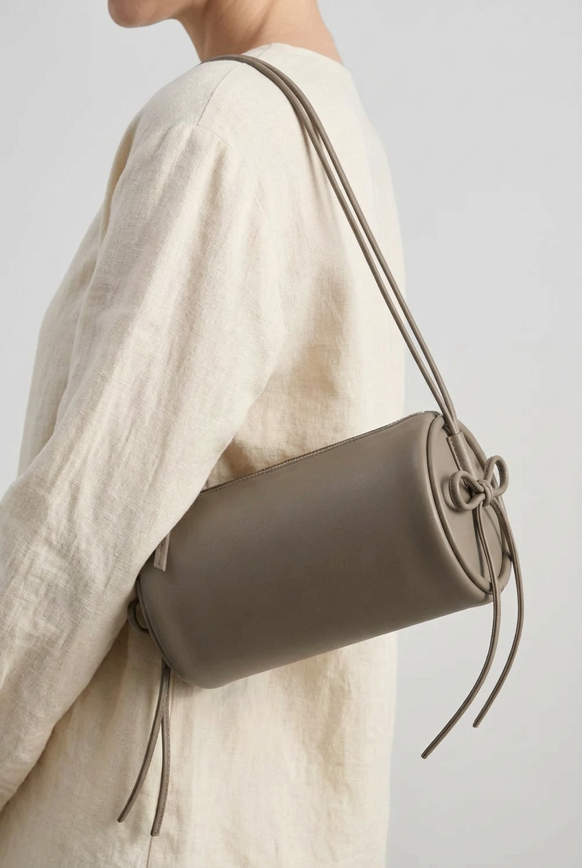 Sac Alma en cuir gris de forme cylindrique, porté à l’épaule, vu de profil avec cordons noués sur le côté