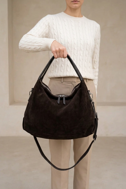 Sac Capucine en cuir velours brun foncé porté à la main, avec fermeture zippée et bandoulière attachée visibles