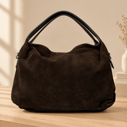Sac Capucine en cuir velours brun foncé posé sur une table en bois clair, avec ses deux anses sombres