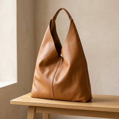 Sac shopper en cuir grainé camel posé sur un banc en bois clair, vu de trois quarts