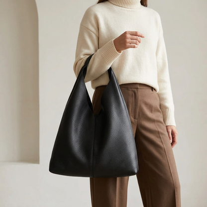 Sac shopper en cuir grainé noir porté à l’avant-bras par une femme en pull écru