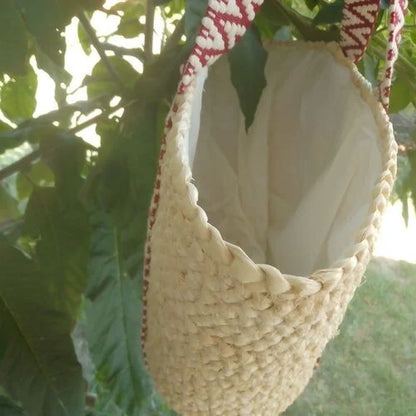 Cabas en raphia beige naturel vu de côté, avec doublure claire et anses à motifs bordeaux et écrus. 